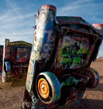 Colorful spray-painted vintage cars buried nose-first at Cadillac Ranch under a blue sky.