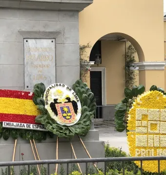 Francisco Pizarro statue pedestal with a plaque, surrounded by wreaths and floral displays in front of a yellow building.