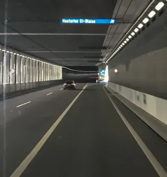 A brightly lit road tunnel with a car driving ahead and an overhead sign for Hauterive St-Blaise.