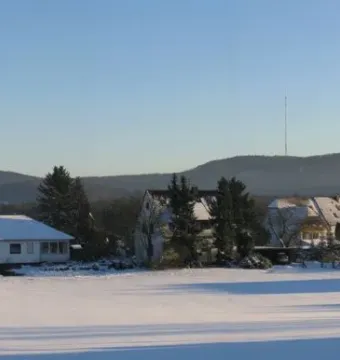 The Hermannsdenkmal appears as a small dark silhouette on a distant forested hill above a snowy landscape with houses in the foreground.