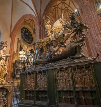 Wooden sculpture of Saint George on horseback slaying a multi-headed dragon, with a crowned female figure beside it.