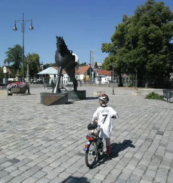 A child with a bicycle stands on a cobblestone plaza facing the Anscavallo horse sculpture.