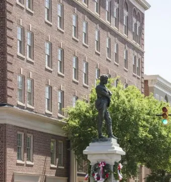 Appomattox bronze statue on a stone pedestal decorated with a red and white wreath at a street intersection.
