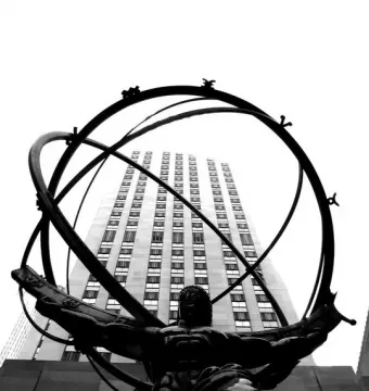 Atlas statue supporting a large armillary sphere with a tall building behind it.