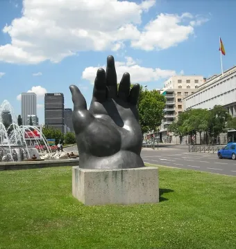 Dark Botero hand sculpture with curled fingers on a concrete plinth.