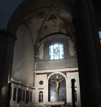 Brunelleschi Crucifix mounted on a dark cross beneath a marble archway, with two visitors in the foreground.