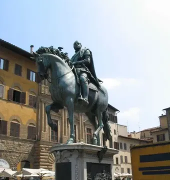 The Cosimo I Equestrian Monument shows a verdigris-patinated armored rider on a rearing horse atop a decorated stone pedestal in a sunny Florence square.