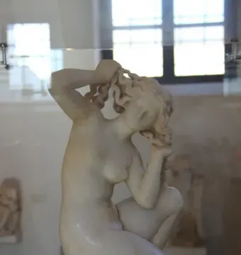 Crouching Venus marble statue in a crouching pose with her head lowered and hands raised to her hair.