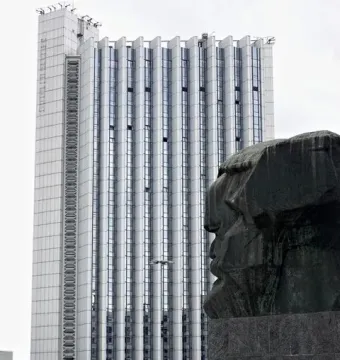 Karl Marx Monument in front of a modern building, with people gathered in the square below.