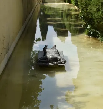 Ophelia Drowned sculpture lying on a submerged base in a shallow green-tinged water channel