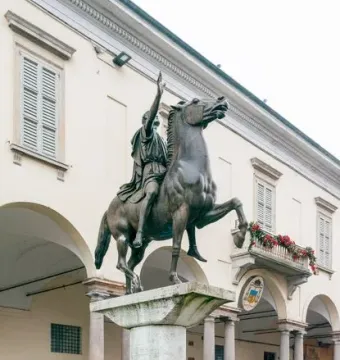 The Regisole bronze equestrian statue stands on a tall stone pedestal in a paved courtyard.