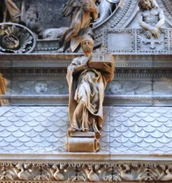 Marble statue of Saint Petronius holding a model of a building within an ornate monument with relief figures and decorative details.