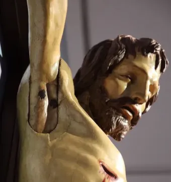 Close-up of the Santa Croce Crucifix showing the upper torso, head, and right arm, with a realistic chest wound and painted blood.