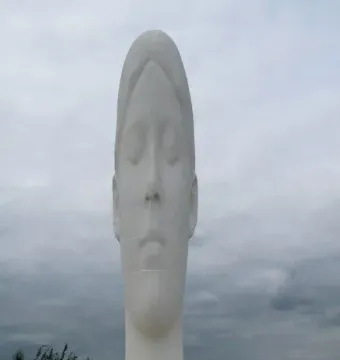 Dream, a tall white sculpture of a serene face with closed eyes, rising above its stepped base with people nearby for scale.