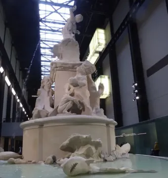 Fons Americanus by Kara Walker, a large white tiered fountain with sculpted figures and sea creatures inside a vast industrial hall.