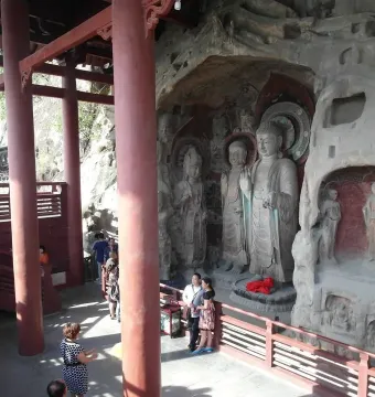 Huangze Monastery rock sculptures carved into cave walls beside a visitor platform with red pillars