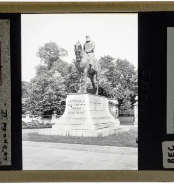 Leopold II equestrian statue on a tall stone pedestal in a park-like setting with trees and a stone balustrade behind it.