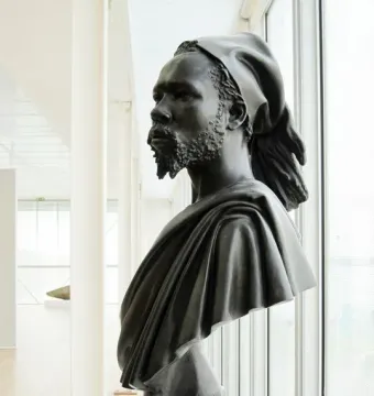 The Nubian Man bronze sculpture of an adult male figure on a white pedestal, shown in three-quarter profile.