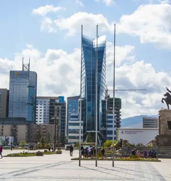 Statue of Damdin Sükhbaatar on a stone plinth in a paved square with tall glass skyscrapers behind it.