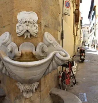 Fontana dello Sprone, a white marble fountain with a grotesque bearded face and conch-shaped basin built into a corner wall.