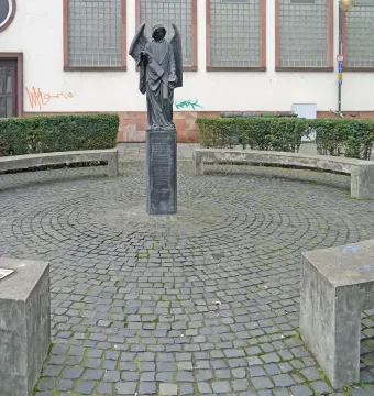 The Frankfurter Engel statue, a dark winged angel holding a scroll, stands on a pedestal in a cobblestone plaza.