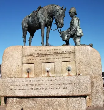 Horse Memorial showing a kneeling uniformed figure offering a pail to a saddled horse on a stone pedestal.