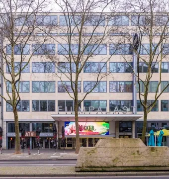 Ruhender Verkehr, a large weathered concrete block sculpture on a city sidewalk beside a building and bare trees.