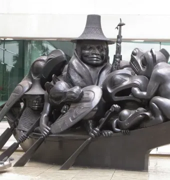 Spirit of Haida Gwaii sculpture showing a dark canoe filled with human and animal figures in a shallow pool