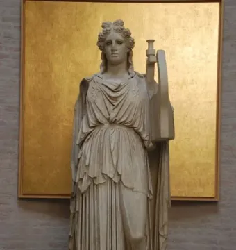 Apollo Barberini marble statue holding a large lyre, displayed against a golden panel on a brick wall.