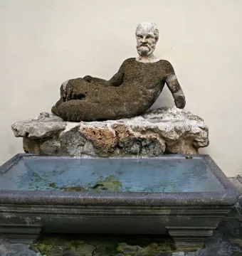 Babuino Fountain with a reclining stone figure over a rectangular basin of greenish water.