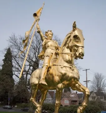 Joan of Arc equestrian statue in golden bronze on a stone pedestal in a park setting.