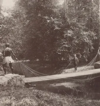 Morianbron with dark human-shaped statues on stone pedestals beside a narrow bridge over a stream in a wooded park.