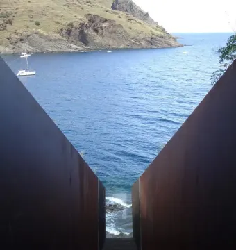 Pasajes memorial with a dark metal chute framed by rusted walls overlooking the sea.