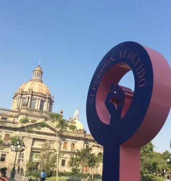 Antimonumenta sculpture shaped like the female gender symbol with a raised fist, set against a cathedral and blue sky.