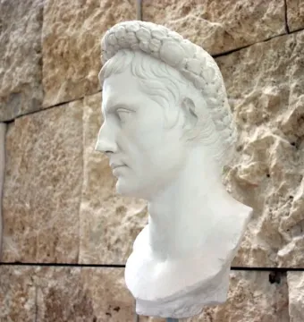 Bust of Augustus wearing a gemmed crown, shown in profile against a stone wall.