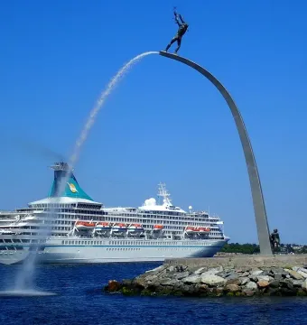 The God our Father on the Rainbow sculpture beside a white cruise ship passing on the water.