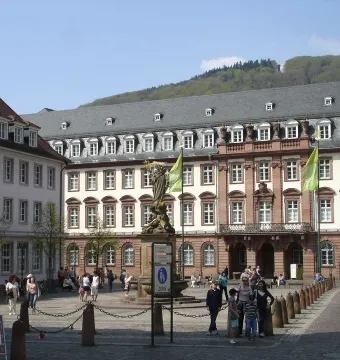 Kornmarkt Madonna on a tiered pedestal in a cobblestone square, with a crowned robed figure holding a smaller figure.