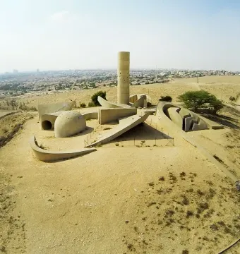 Aerial view of the Negev Brigade Monument, a large concrete memorial with a tall cylindrical tower and curved walls on a dry hilltop.
