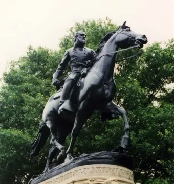 Stonewall Jackson equestrian statue on a stone pedestal with carved figures and trees behind it