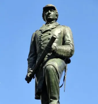 Admiral David G. Farragut statue in bronze with a green patina, holding a telescope against a blue sky.