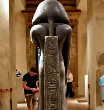 Back view of the Amenemhat III statue with a pleated nemes headdress and inscribed back pillar in a museum gallery.
