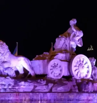 The Cibeles Fountain at night, lit in purple with water spraying from the fountain.