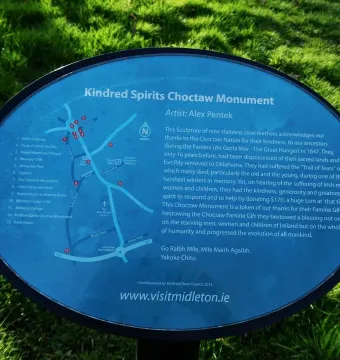 Blue informational plaque for the Kindred Spirits Choctaw Monument with white text and a small map beside grass.