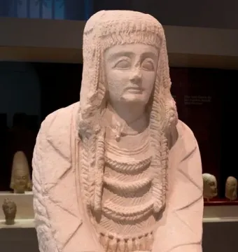 Lady of Cerro de los Santos statue holding a small vessel, with an elaborate braided headdress and layered necklaces.