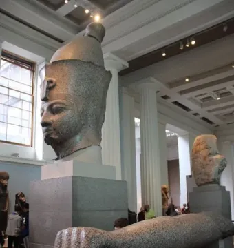 Colossal Head of Amenhotep III with a speckled stone arm displayed on supports in the foreground.