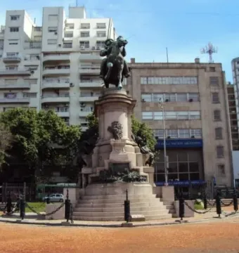 Bronze equestrian monument to Giuseppe Garibaldi on a tall stone pedestal in a city plaza, with trees and surrounding buildings.