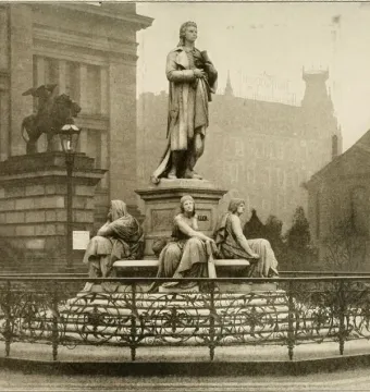 Schiller Monument with a standing man at the center, surrounded by three allegorical female figures and an ornate fence.