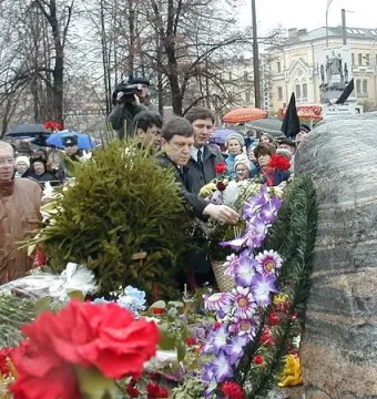 Solovetsky Stone covered with floral wreaths and bouquets as people gather around the memorial.