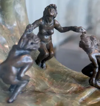 Three dark bronze nude figures holding hands on The Wave sculpture with a curling marbled stone base.