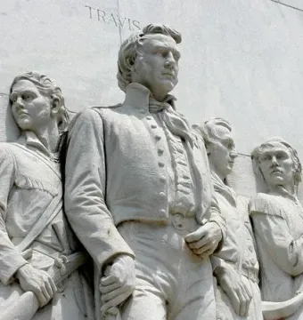 Relief figures on the Alamo Cenotaph with the names Travis and Crockett etched in the stone.